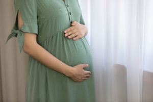pregnant person wearing a green dress, holding their stomach at a reproductive health clinic in Boul